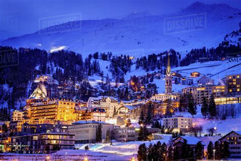 Village Beneath Mountain On Snow Covered Landscape Illuminated In The