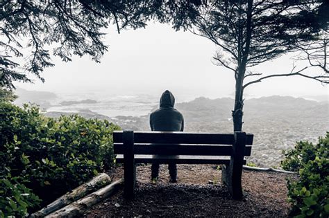 Sad And Lonely Man Sitting On Bench Overlooking Sea On Vancouver Island