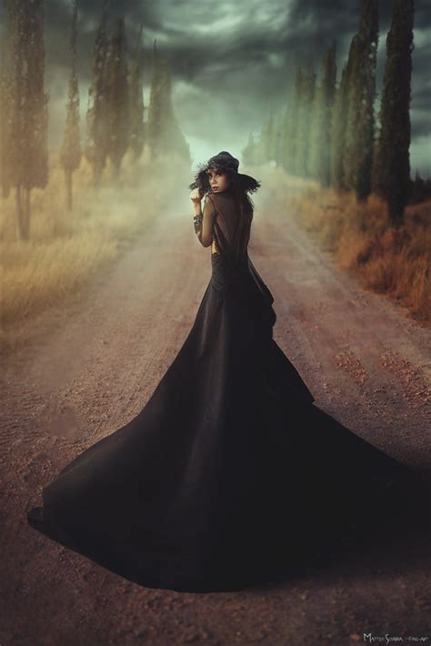 Фото Девушка в длинном черном платье и шляпе стоит на дороге By Matteo