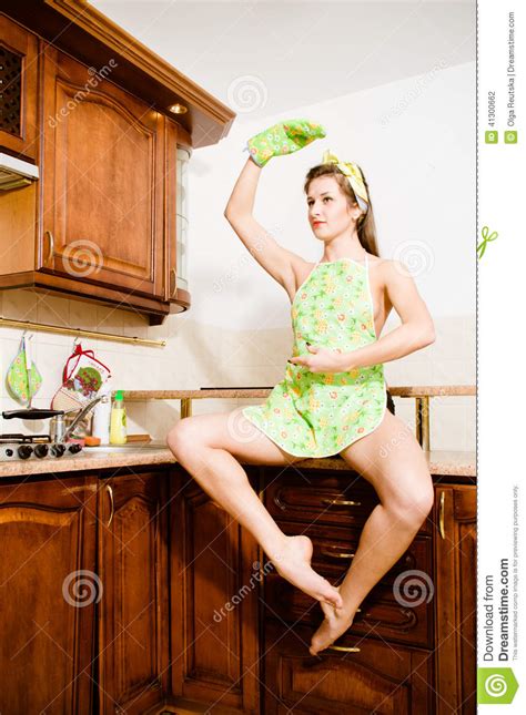 Dancing Girl Sitting On The Table In The Kitchen Apron Hand Up Looking