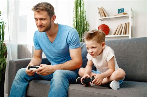 Padre Y Su Pequeño Hijo Jugando Videojuegos Juntos En El Sofá En Casa
