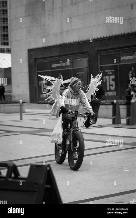 A Vertical Grayscale Of A Man Riding A Bike Wearing Angels Wings In