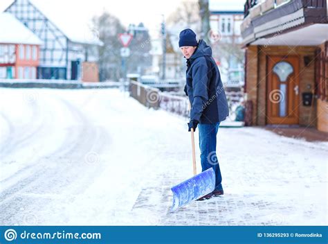 Man With Snow Shovel Cleans Sidewalks In Winter During Snowfall Winter