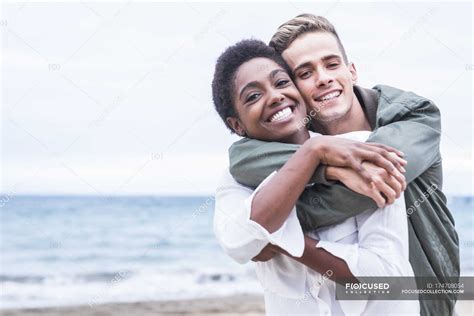 Счастливая молодая пара обнимается на пляже и смотрит в камеру — Радость Женский пол Stock