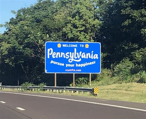 A Welcome To Pennsylvania Sign On The Side Of A Road With Trees In The