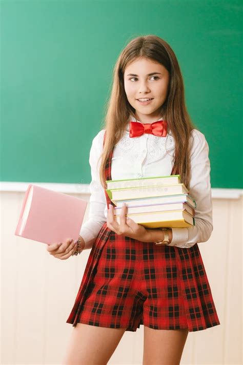 Schönes Schulmädchen In Der Roten Schuluniformstellung Mit Büchern Vor Der Tafel Stockbild