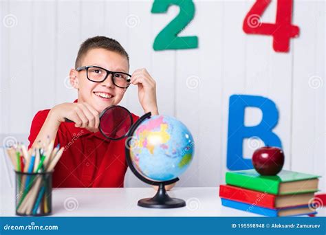 Happy Cute Clever Boy Is Sitting At A Desk In A Glasses With Raising