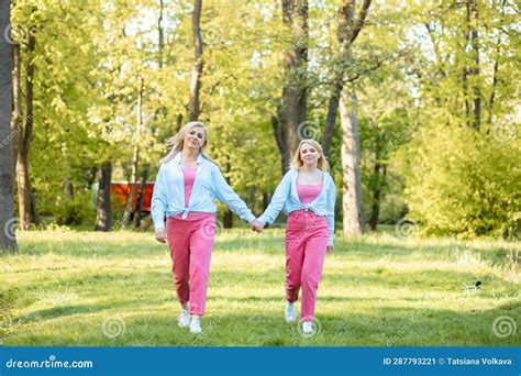 Charming Blonde Mom And Her Adult Daughter Dressed In Same Clothes Walk Hand In Hand Step By