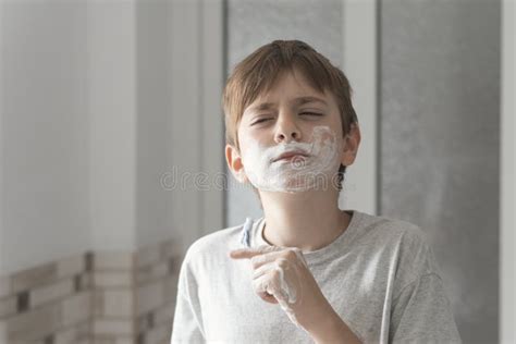 Little Boy Smears Shaving Foam On Face Looks In Mirror With Serious