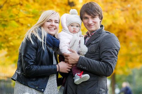 Happy Parents Holding Daughter On Arms In Autumn Park Stock Image
