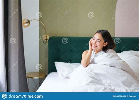 Beautiful Sleepy Asian Girl Wakes Up In Her Bed With Cozy White Blankets Looking Outside Window