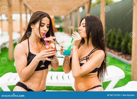 Two Beautiful Women Having Cocktails Together By The Swimming Pool