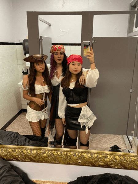 Three Women Dressed Up In Costumes Taking A Selfie In A Bathroom Mirror