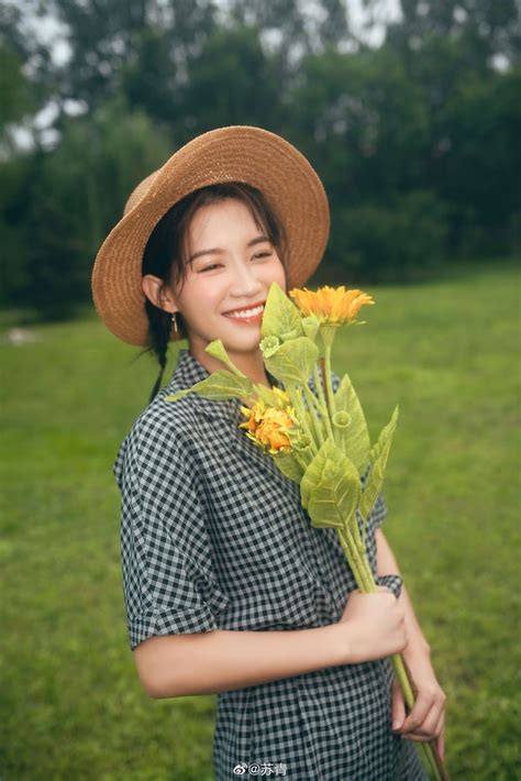 A Woman In A Hat Holding Flowers And Smiling At The Camera While