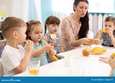 Children And Carer Together Eat Fruit As A Snack In The Kindergarten