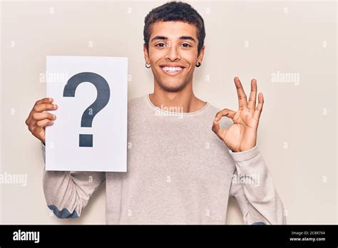 Young African Amercian Man Holding Question Mark Doing Ok Sign With
