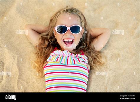 Top View Of Pretty Little Blonde Girl In Sunglasses Lying On Sandy Beach During Summer Vacation