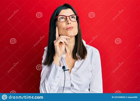 Young Hispanic Woman Using Lavalier Microphone Serious Face Thinking