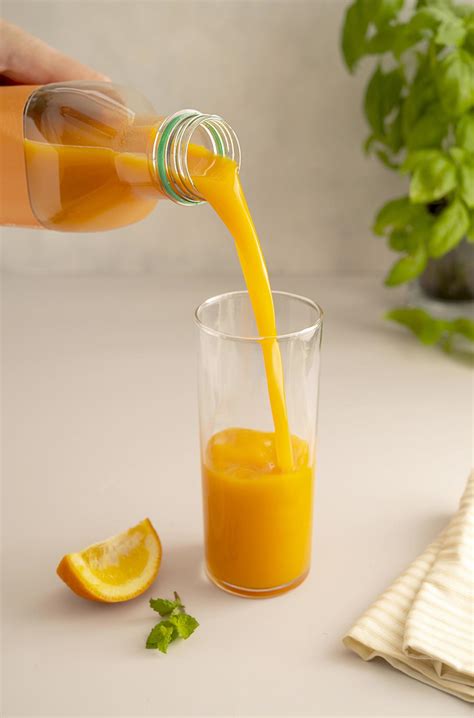 jugo de naranja saliendo de una botella de plástico en vidrio aislado en un fondo brillante