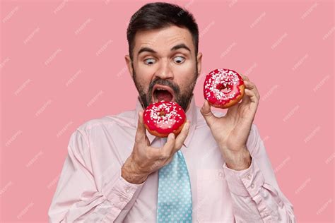 Free Photo Hungry Handsome Man Bites Red Doughnut Wears Formal Shirt