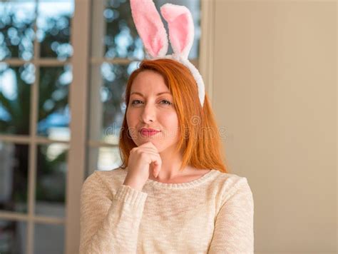 redhead woman wearing easter rabbit ears at home serious face thinking about question very