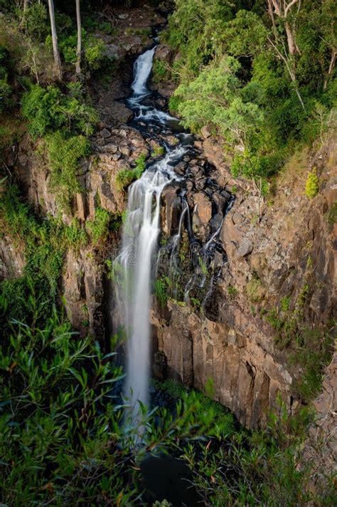 A Tall Cascading Waterfall Surrounded By Lush Greenery And Rocky