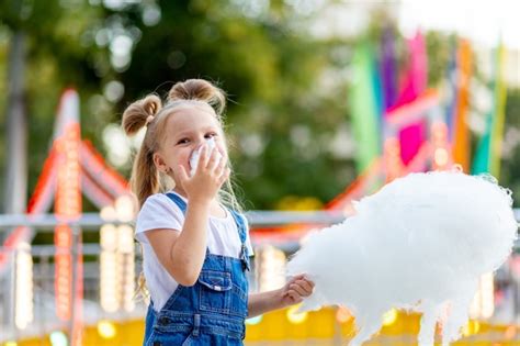 niña feliz comiendo algodón de azúcar en el parque de atracciones foto premium