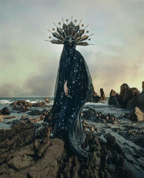 A Woman With A Crown On Her Head Is Standing On Rocks Near The Ocean
