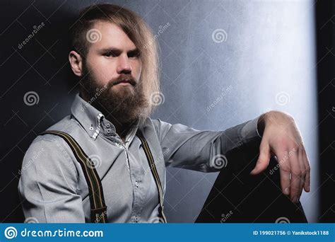 A Portrait Of An Attractive Brooding Bearded Man Sitting Against A Wall