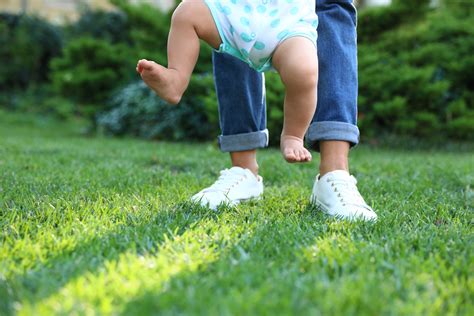 Cute Little Baby Learning To Walk With His Nanny On Green Grass