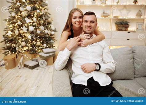 Couple In Love Kisses And Hugs On The Sofa Near The Christmas Tree Lights New Year`s Night