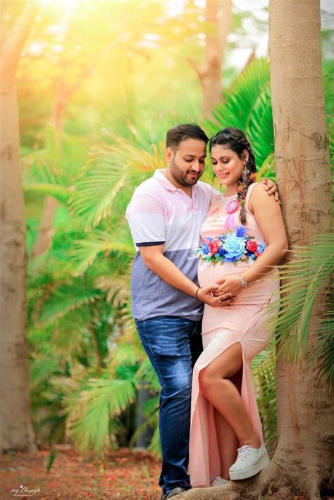A Pregnant Couple Standing Next To Each Other In Front Of Palm Trees