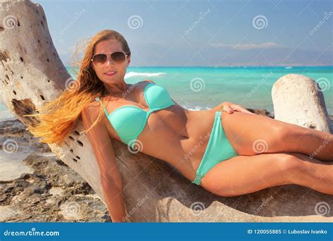 Woman In Cyan Blue Bikini And Sunglasses Laying On The Drift Wood Tree With Turquoise Sea