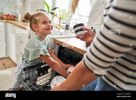 Daughter Helping Mother Arranging Crockery In Dishwasher Stock Photo