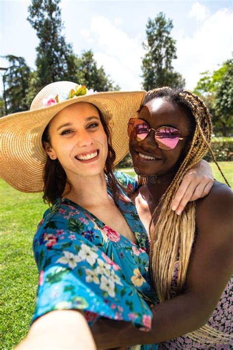 Smiling And Happy Young Multiracial Female Couple Take Selfie In The Park In Summertime Stock