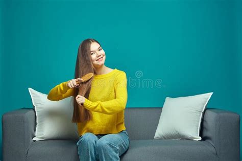 Smiling Girl Brush Healthy Glossy Long Hair By Hairbrush Preening Sitting On Sofa Haircare