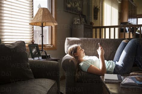 Happy Girl Lying On Sofa And Using Phone In Living Room Stock Photo
