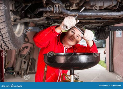 Handsome Male Car Mechanic In Uniform Working Underneath A Lifted Car
