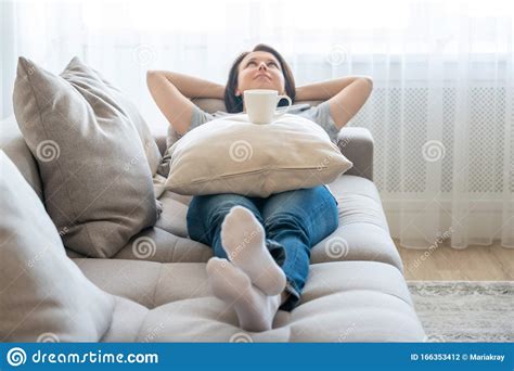 Young Woman Relaxing On Her Couch With Cup Of Coffee On A Pillow Stock