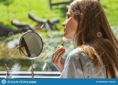 A Beautiful Girl Does A Facial Massage With A Roller At Home In Front Of A Mirror Facial Skin