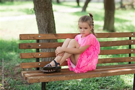 Little Caucasian Girl Sitting In Park On Bench A Child In A Beautiful