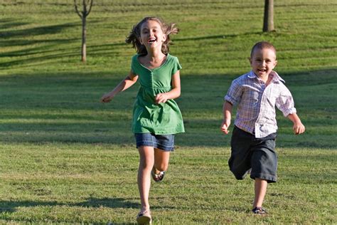 Two Happy Little Kids Having Fun While Running Through The Grassy Field