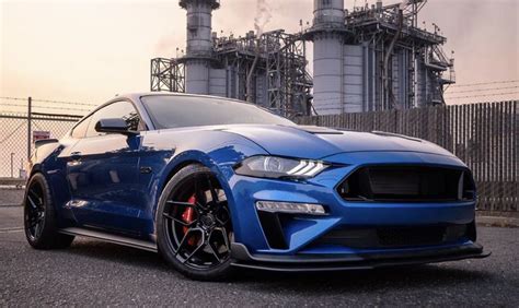 A Blue Mustang Parked In Front Of An Industrial Plant