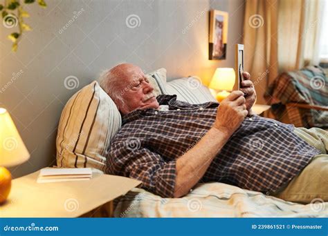 Old Man In Casualwear Lying On Bed And Looking At Picture Of His Wife
