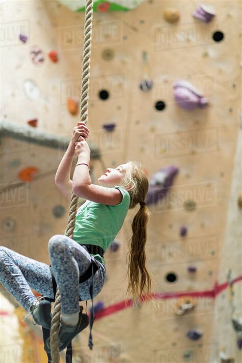 Caucasian Girl Climbing Rope On Rock Wall Indoors Stock Photo Dissolve