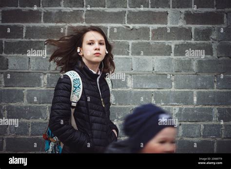 Schoolgirl With Backpack With Flying Hair And Headphones Against Gray Brick Wall With Copy Space