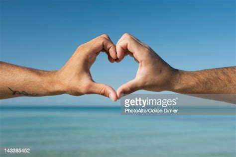 Two Mens Hands Forming Heart Shape By Ocean Cropped High Res Stock