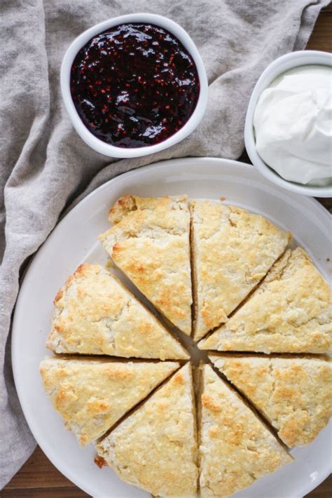 A White Plate Topped With Scones Next To A Bowl Of Whipped Cream And A