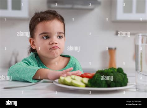 Cute Little Girl Refusing To Eat Vegetables In Kitchen Stock Photo Alamy