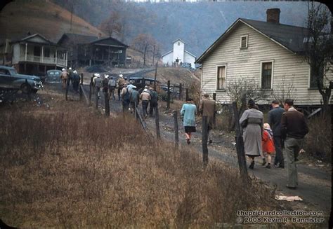 Many People Are Walking On The Side Of A Road In Front Of An Old House